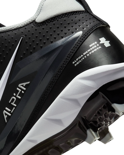 Primer plano del taco Nike Alpha Menace Varsity 4 en negro y blanco con detalles de agilidad y potencia visibles en la suela y lateral.